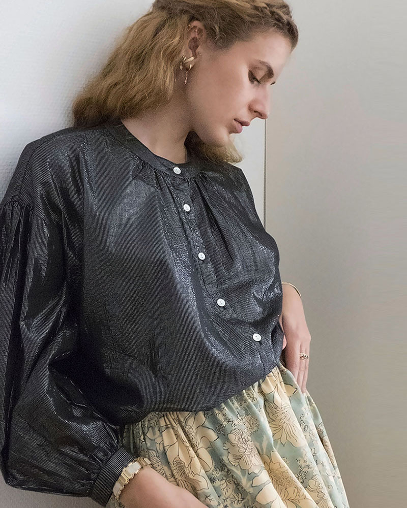 Blouse bohème Billie en coton et lurex noir, avec patte de boutonnage à petits boutons nacrés, fronces à l'encolure et manches amples, portée avec une jupe fleurie